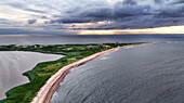 Luftaufnahme eines ruhigen Küstenabschnitts, wo das üppige Grün der Insel auf den weiten Ozean unter einem dramatischen Himmel trifft, New Shoreham, Rhode Island, Vereinigte Staaten.