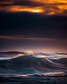 Blick auf die Wellen des Ozeans, die unter einem dramatischen Himmel mit orangefarbenen Wolken, die auf den dunklen Horizont treffen, heftig schlagen, Kapstadt, Westkap, Südafrika.