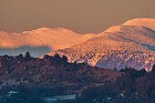 Aerial view of snow-covered mountains kissed by the warm glow of the setting sun, casting long shadows across the landscape, Oravce, Banská Bystrica Region, Slovakia.