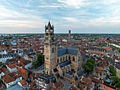 Aerial view of the towering Church of Our Lady, its spire piercing the soft sky above the red-tiled rooftops of the medieval city, Bruges, Flanders, Belgium.