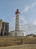 View of the majestic Saint-Mathieu Lighthouse stands tall with its red and white stripes, against the backdrop of aged stone ruins, Plougonvelin, Bretagne, France.