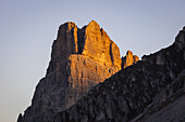 Blick auf einen majestätischen Berggipfel, der in das warme Licht der untergehenden Sonne getaucht ist und einen starken Kontrast zum schattigen Vordergrund bildet, Cortina d'Ampezzo, Belluno, Italien.