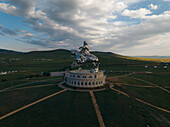 Aerial view of the gleaming silver Chinggis Khaan Statue on its circular base, reflecting the blue sky above the vast green Mongolian steppe, Ulaanbaatar, Mongolia.