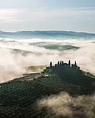 Aerial view of a hilltop village shrouded in mystical fog, the Tuscan landscape painted in hues of green and gold, San Quirico d'Orcia, Tuscany, Italy.