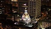 Aerial view of the illuminated dome atop a historic building with the American flag waving proudly against the night sky, Savannah, Georgia, United States.