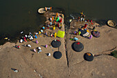 Hampi, India - 30 December 2010: Aerial view of women in vibrant saris washing clothes on sun-baked rocks beside the Tungabhadra River, colors contrasting with the earthy tones.