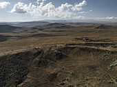 Luftaufnahme der trockenen Landschaft, ein Wandteppich aus Braun- und Brauntönen, unterbrochen von Felsen unter einem weiten Himmel, Vardenyats Pass, Vayots Dzor, Armenien.