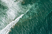 Aerial view of the ocean's turquoise expanse meeting the shore with foamy white waves crashing against the deep blue, Princetown, Victoria, Australia.