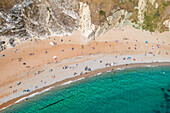 Aerial view of the turquoise sea meeting the sandy beach, backed by chalk cliffs, a vibrant scene of summer leisure, Wareham, England, United Kingdom.