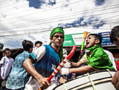 Chattogram, Bangladesch - 29. Juli 2023: Blick auf einen Mann mit grünem Stirnband, der einen Stock hält, und ein Kind in einem grünen Hemd, das neben einer Trommel schreit.