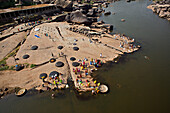 Hampi, India - 30 December 2010: Aerial view of women in vibrant saris washing clothes on the riverbank against the backdrop of ancient stone structures.