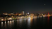 Aerial view of the city's vibrant waterfront, where lights dance on the water reflecting the illuminated skyline under the soft glow of the moon, Savannah, Georgia, United States.