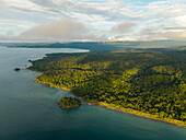 Aerial view of the lush, dense jungle meeting the deep blue sea, a small island off the coast under soft clouds, Nuquí, Choco, Colombia.