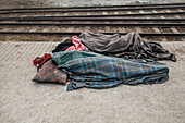 Tongi, Bangladesh - 02 February 2025: View of a person sleeping on a railway platform with blankets and a pillow, juxtaposed against the stark, converging lines of the train tracks.