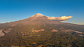 Luftaufnahme des majestätischen Berges Fuji, dessen schneebedeckter Gipfel in einen ruhigen blauen Himmel ragt und an dessen Seite sich eine einsame Wolke festhält, Kamiide, Shizuoka, Japan.