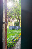 Tuscany, Italy - 23 April 2025: View of a tranquil garden bathed in sunlight, with modern outdoor furniture nestled among vibrant flowerbeds and lush trees.