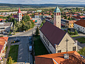 Aerial view of the church tower rising above the town, contrasting with the red roofed church and autumnal hues of the landscape, Pukanec, Nitra Region, Slovakia.