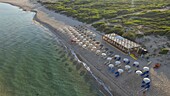 Luftaufnahme von sonnenverwöhnten Sandstränden, die auf das ruhige türkisfarbene Wasser der Küste treffen, mit ordentlichen Reihen von Sonnenschirmen und einer Struktur am Strand, Sardinien, Italien.