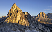 Luftaufnahme von zerklüfteten Gipfeln, die in das warme Licht des Sonnenaufgangs getaucht sind und starke Schatten auf das felsige Gelände des Passo Giau, Cortina d'Ampezzo, Belluno, Italien, werfen.