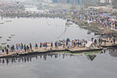 Tongi, Bangladesh - 31 January 2025: Aerial view of crowds crossing the murky river on makeshift platforms, a scene of bustling activity against the urban backdrop.