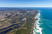 Luftaufnahme der zerklüfteten Klippen von Princetown, die auf den türkisfarbenen Ozean treffen, das Land ein Flickenteppich aus Grün und Braun unter einem weiten blauen Himmel, Princetown, Victoria, Australien.