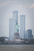 Blick auf die Freiheitsstatue, ein Leuchtfeuer der Freiheit, vor dem Hintergrund moderner Wolkenkratzer unter einem blassen Himmel, New York, New York, Vereinigte Staaten.