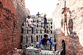 Narsingdi, Bangladesch - 08. Dezember 2024: Blick auf Arbeiter inmitten von hoch aufgetürmten Ziegelstapeln, deren Arbeit sich von den verwitterten Ziegelwänden abhebt, eine Szene von Industrie und menschlicher Anstrengung.