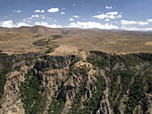 Luftaufnahme von steilen Klippen, die in eine grüne Schlucht abfallen, in der die raue Schönheit der Natur mit der trockenen Landschaft kontrastiert, Goght, Provinz Ararat, Armenien.