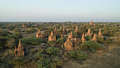 Luftaufnahme von alten Tempeln, die sich majestätisch aus der grünen Landschaft erheben und deren verwitterte Fassaden sanft im sanften Licht leuchten, Alt-Bagan, Region Mandalay, Myanmar.