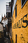 View of a narrow cobblestone street with a stream flowing beside old buildings, including a yellow structure with 'SALZHAUS' written on it, Hallstatt, Austria.