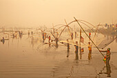 Pabna, Bangladesh - 28 November 2023: View of many fishermen with their nets standing in the water creating a golden, misty scene at Pabna..
