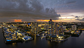 Luftaufnahme von beleuchteten Gebäuden, die sich auf dem Wasser spiegeln, unter einem dramatischen Himmel mit feurigen Farbtönen am Horizont, Aventura, Florida, Vereinigte Staaten.