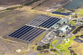 Aerial view of long, dark rectangular pools contrasting with the light-colored landscape, next to industrial buildings and smaller ponds, Breamlea, Victoria, Australia.