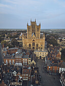 Aerial view of the grand Lincoln Cathedral rising majestically above the quaint rooftops of the city, a symphony of golden stone against the tranquil sky, Lincoln, England, United Kingdom.