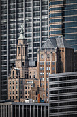 Blick auf ein altes Gebäude mit hellbrauner Steinfassade und grünem Kirchturm, eingerahmt von modernen Wolkenkratzern aus Glas und Stahl, New York, New York, Vereinigte Staaten.