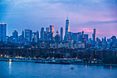 Blick auf die Skyline der Innenstadt von Manhattan, die im letzten Licht des Sonnenuntergangs erstrahlt und sich im ruhigen Wasser des Flusses spiegelt, ein lebendiges Stadtbild, New York, New York, Vereinigte Staaten.
