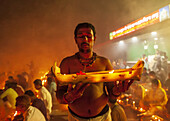Narayanganj, Bangladesh - 15 November 2022: View of a man holding a candlelit offering, surrounded by a crowd bathed in warm, ethereal light near a brightly lit building.