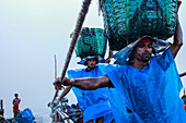 Chattogram, Bangladesh - 28 November 2019: View of laborers in blue raincoats carrying heavy turquoise baskets amidst the overcast sky, a scene of resilience and hard work.