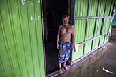 Noakhali, Bangladesh - 07 September 2024: View of a man standing at the entrance of a green corrugated metal structure, the muddy floodwater reflecting the somber mood.