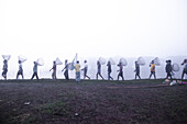 Pabna, Bangladesh - 28 November 2023: View of men walking along the riverbank carrying fishing nets, their silhouettes fading into the misty horizon.