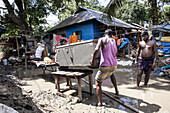 Feni, Bangladesh - 29 August 2024: View of men wading through floodwaters, salvaging a large metal container near a blue-roofed house amidst the devastation.
