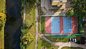 Aerial view of a vibrant sports court, where blue and red hues meet amidst lush greenery, adjacent to a tranquil canal, Bydgoszcz, Województwo kujawsko-pomorskie, Poland.