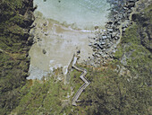 Aerial view of a hidden beach where emerald waters meet the rugged coastline, accessed by a serpentine wooden staircase winding through verdant slopes, Cala Sonreiras, Cedeira, A Coruña, Spain.