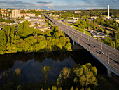 Aerial view of the bridge crossing the dark river, contrasting with the bright green trees and the cityscape in the background, Vilnius, Vilnius, Lithuania.