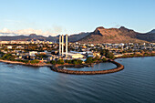 Aerial view of a towering industrial structure standing tall against the backdrop of jagged mountains and a tranquil sea, Port Louis, Port Louis District, Mauritius.