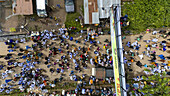 Aerial view of a multitude of people gathering in a vibrant outdoor space near buildings, shaded by trees, under the open sky, Osun-Osogbo, Osun, Nigeria.