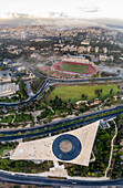 Aerial view of the National Library's modern, angular architecture contrasting with the green sports fields and the cityscape fading into the misty horizon, Jerusalem, Israel.