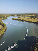Aerial view of boats moored along the riverbank, their white hulls gleaming against the dark water, bordered by green trees and fields, Presqu'île de Conleau, Bretagne, France.