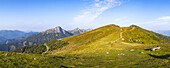 Blick auf sonnenbeschienene Berggipfel, die sich dem blauen Himmel entgegenstrecken, ein verschlungener Pfad lockt Abenteurer in den Goldeck-Bergen, Goldeck, Kärnten, Österreich.