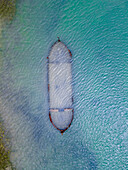 Luftaufnahme eines Schiffswracks im türkisfarbenen Wasser, das als gespenstische Erinnerung an die Geschichte der Seefahrt still auf dem Meeresgrund ruht, Chiclana de la Frontera, Andalusien, Spanien.